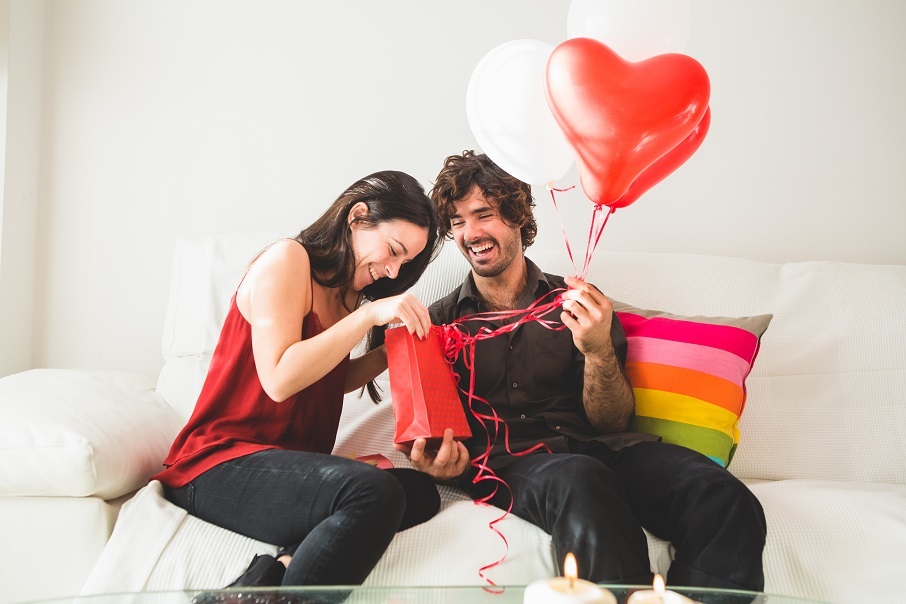 young-girl-looking-red-bag-while-her-boyfriend-holds-red-white-balloons